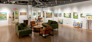 Art gallery with green sofas, brown chairs, and colorful paintings on white walls.